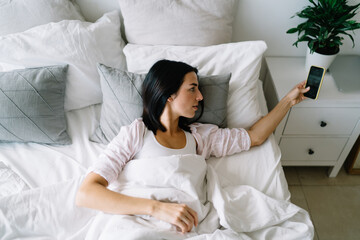 Young woman lying in bed looking at smartphone on bed