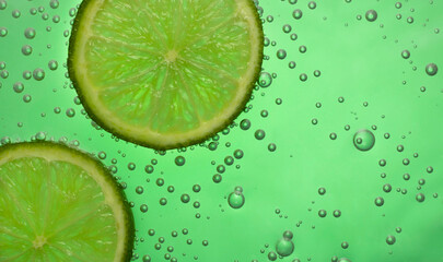 Fototapeta na wymiar lime slices close-up in water with bubbles on a green background