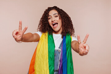 Portrait of cheerful arabic woman with curly hair in multi color rainbow flag at studio isolated...