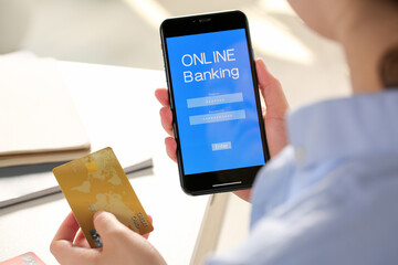 Woman using online banking app on smartphone and credit card at white office table, closeup