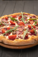 Pizza with salami, arugula, and vegetables on dark wooden background.