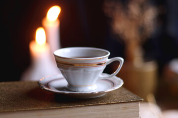 Stack of vintage books, cup of tea or coffee, lit candles, reading glasses and chess pieces on wooden table. Dark academia concept. Selective focus.