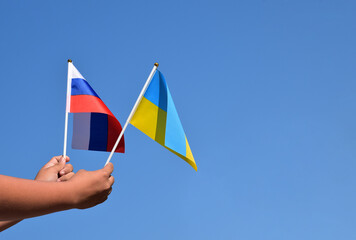 Russian national flag and Ukrainian national flag holding in hands against bluesky background, soft and selective focus.