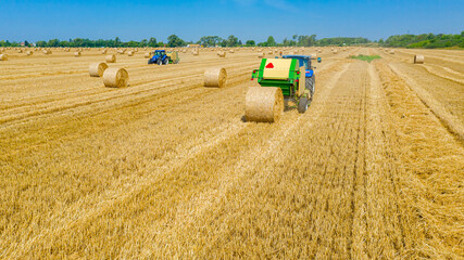 Aerial view of tractor tow trailed bale machine to collect straw from harvested field