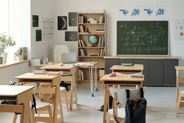 Empty classroom of algebra or physics subject with formulas written on blackboard and rows of desks...