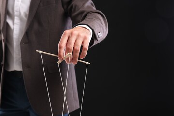 Man in suit pulling strings of puppet on black background, closeup. Space for text