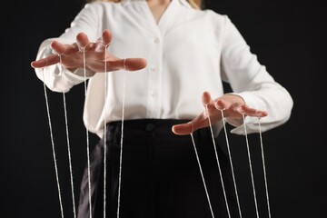 Woman in formal outfit pulling strings of puppet on black background, closeup