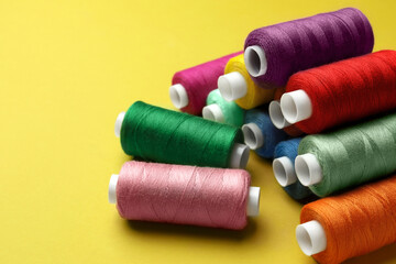 Different colorful sewing threads on yellow background
