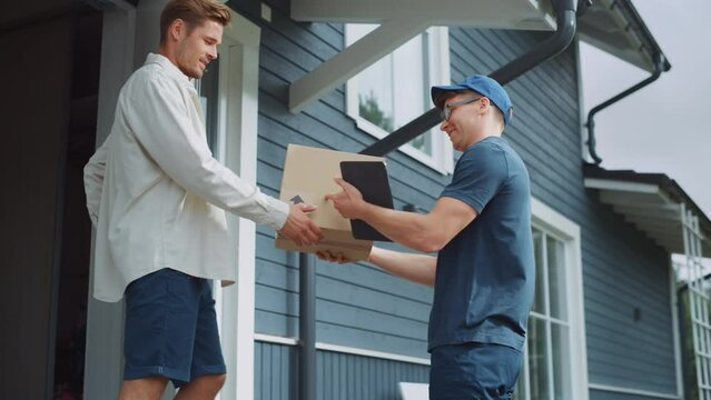 Low Angle Portrait of a Young Mailman Bringing a Cardboard Parcel to a Residential Area House. Handsome Homeowner Greeting the Employee, Leaving a Signature on a Device and Wishing Good Bye.
