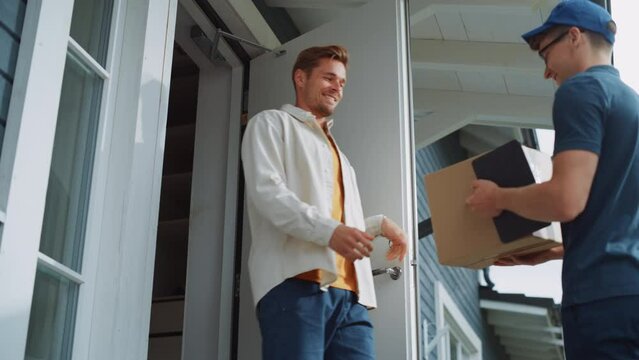 Portrait of a Handsome Young Homeowner Receiving an Awaited Parcel from a Cheerful Mailman. Postal Service Worker Comes to the House to Make a Door to Door Delivery and Get a POD Signature on Tablet.