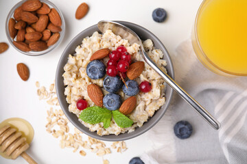 Oatmeal served with berries, almonds and honey on white table, flat lay