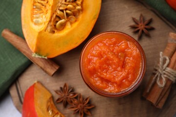 Jar of delicious pumpkin jam and ingredients on wooden board, flat lay
