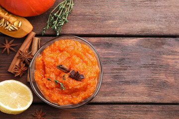 Bowl of delicious pumpkin jam and ingredients on wooden table, flat lay. Space for text