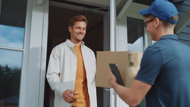 Portrait of a Young Attractive Recipient Opening a Door to a Mailman Bringing a Parcel Box. Postal Service Worker Comes to the House to Make a Delivery and Get a Client's Signature on Tablet Computer.