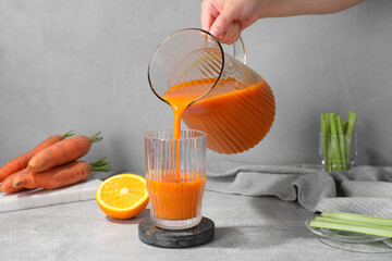 Woman pouring carrot juice from jug into glass at light grey table, closeup