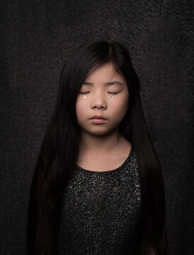 moody fine art painterly portrait of asian girl with silver tear in black dress
