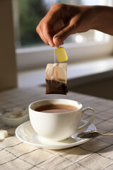 Woman taking tea bag out of cup at table indoors, closeup