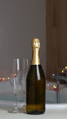 Bottle of champagne, glasses and burning candles near jacuzzi in bathroom