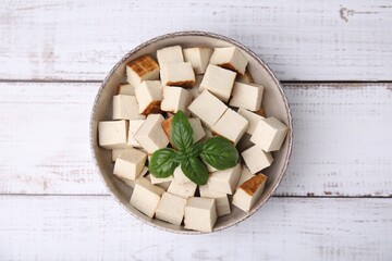 Bowl with delicious smoked tofu and basil on white wooden table, top view