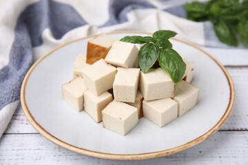 Plate with delicious smoked tofu and basil on white wooden table, closeup