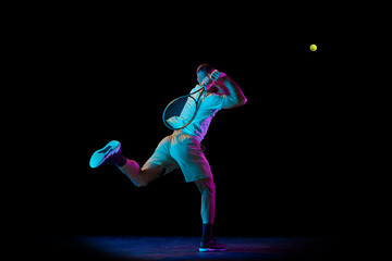 Young sportive man, professional tennis player in motion, action isolated over dark background in neon light. Concept of professional sport, competition, skills.