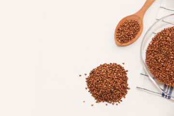 small grains of natural brown buckwheat in a wooden spoon and a glass plate