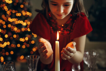 atmospheric, christmas photo, candle burning, children's hands nearby, girl's hands, christmas lights, garland in the background	