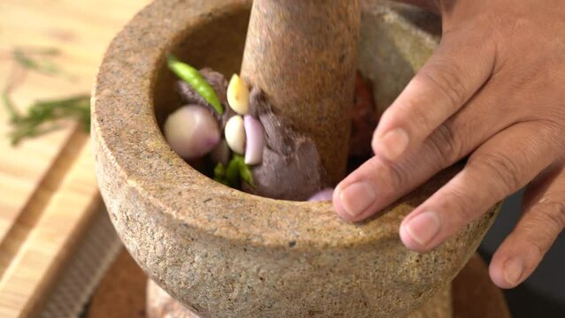 Chef pounding Spicy shrimp paste in a brown stone mortar.