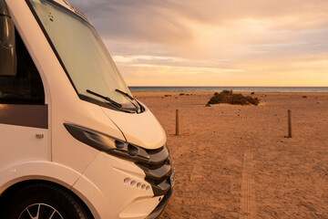 Modern camper van motor home in free adventure parking. Concept of renting camping car vehicle for alternative free off grid van life life vacation. Sunset and beach with amazing sky in background