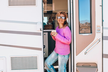 Happy female tourist standing at the door of her camper van enjoying travel and freedom...