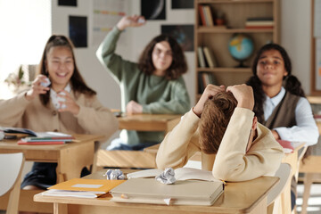 Discriminated schoolboy covering his head while defending from group of cruel classmates throwing...
