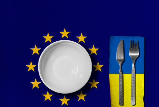 Empty plate on the background of the EU flag. Knife and fork on the background of the flag of Ukraine. Global crisis, food problem. Conceptual message, the problem of hunger and starvation.