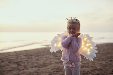 Cute little child girl standing on the sand beach near the sea during sunset with led glowing wings - 543182985