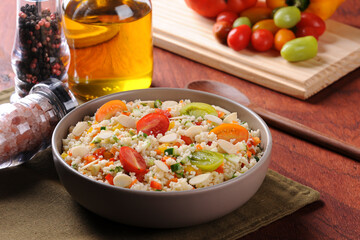 Couscous with vegetables in a rustic bowl surrounded by tomatoes, peppers and a glass of olive oil....