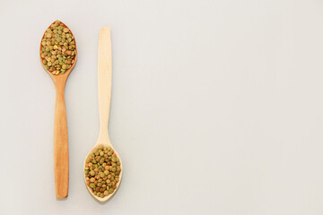 small grains of natural green lentils in a wooden spoon on a gray background