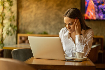 Young beautifull business woman working on laptop in cafe, looking worried