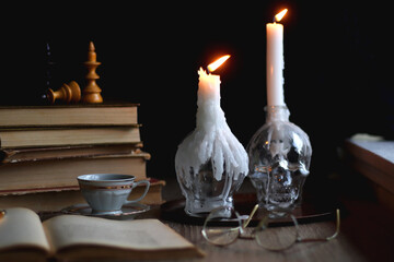 Stack of vintage books, cup of tea or coffee, lit candles, reading glasses and chess pieces on...