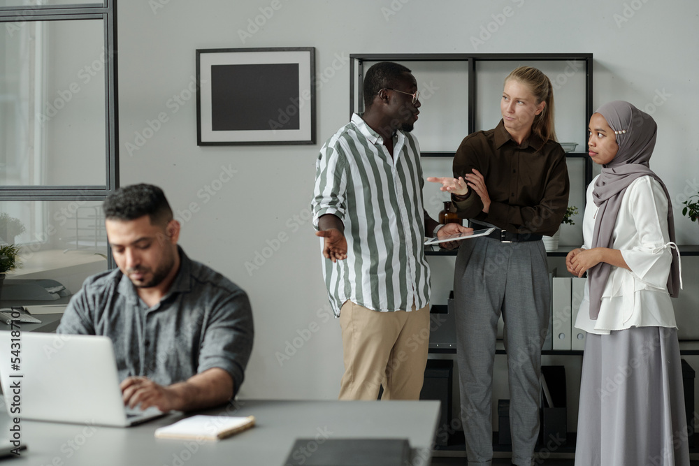 Aufkleber group of young multicultural colleagues talking about hispanic male coworker networking by desk whil