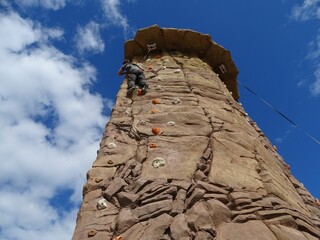Low angle shot of a person doing bouldering on a rock wall under a blue sky