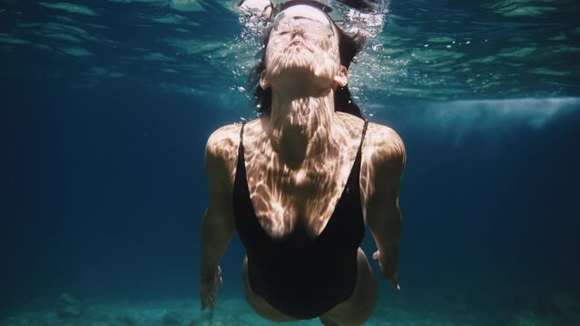 Slow motion close up shot of girl in swimming body suit swimming underwater air bubbles coming out of her nose