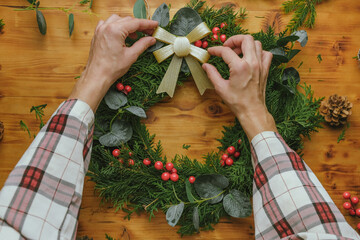 Female hands decorate Christmas wreath with ribbon and bow.