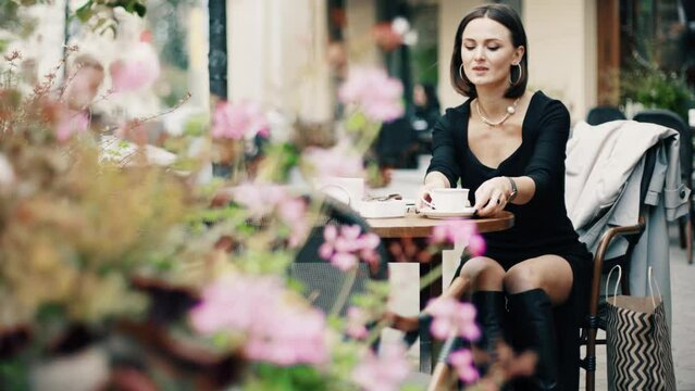 Beautiful brunette woman sitting on outdoor terrace. Caucasian female drinking coffee in the restautant. Slylish lady in bistro.