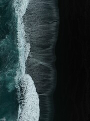 Vertical aerial top view of dark sea waves coming onto the shore