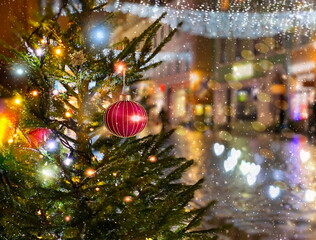 Obraz na płótnie Canvas Christmas red ball festive holiday street decoration green tree branch people walk with umbrella evening blurred light medieval city Talluinn old town