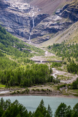 Waterfall and river in the mountains flowing into a turquoise lake. Swiss Alps scenery view, late spring as seen from Bernina Express train.