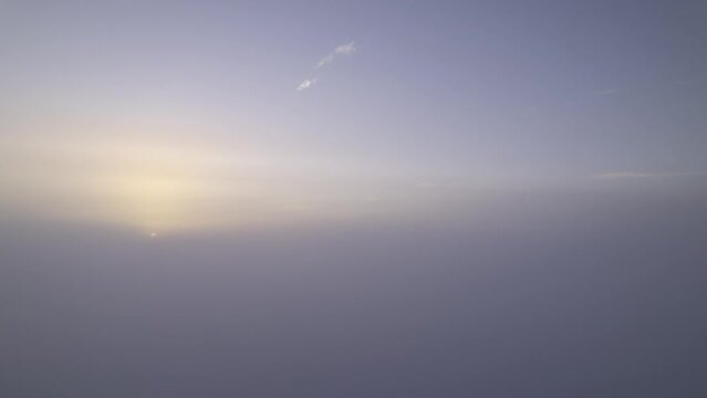 Aerial time lapse shot of the rising sun shining through clouds and fogs at the bottom with blue sky above