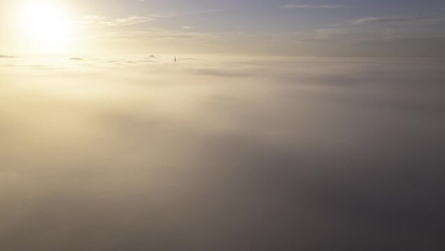 Aerial time lapse shot of the top of Ulm minster sticking through a sea of clouds while sun is rising on a morning in autumn