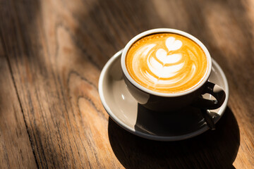 Cup of latte on a wooden table in a beautiful cafe with light from the window.