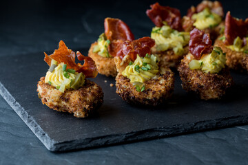 Deep fried deviled eggs on a black slate board against a black background.