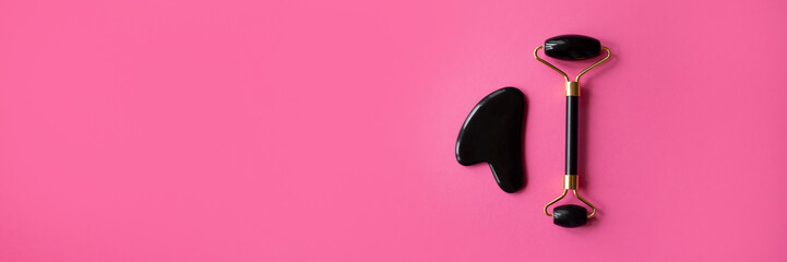 Black gua sha scraper and roller on pink background banner